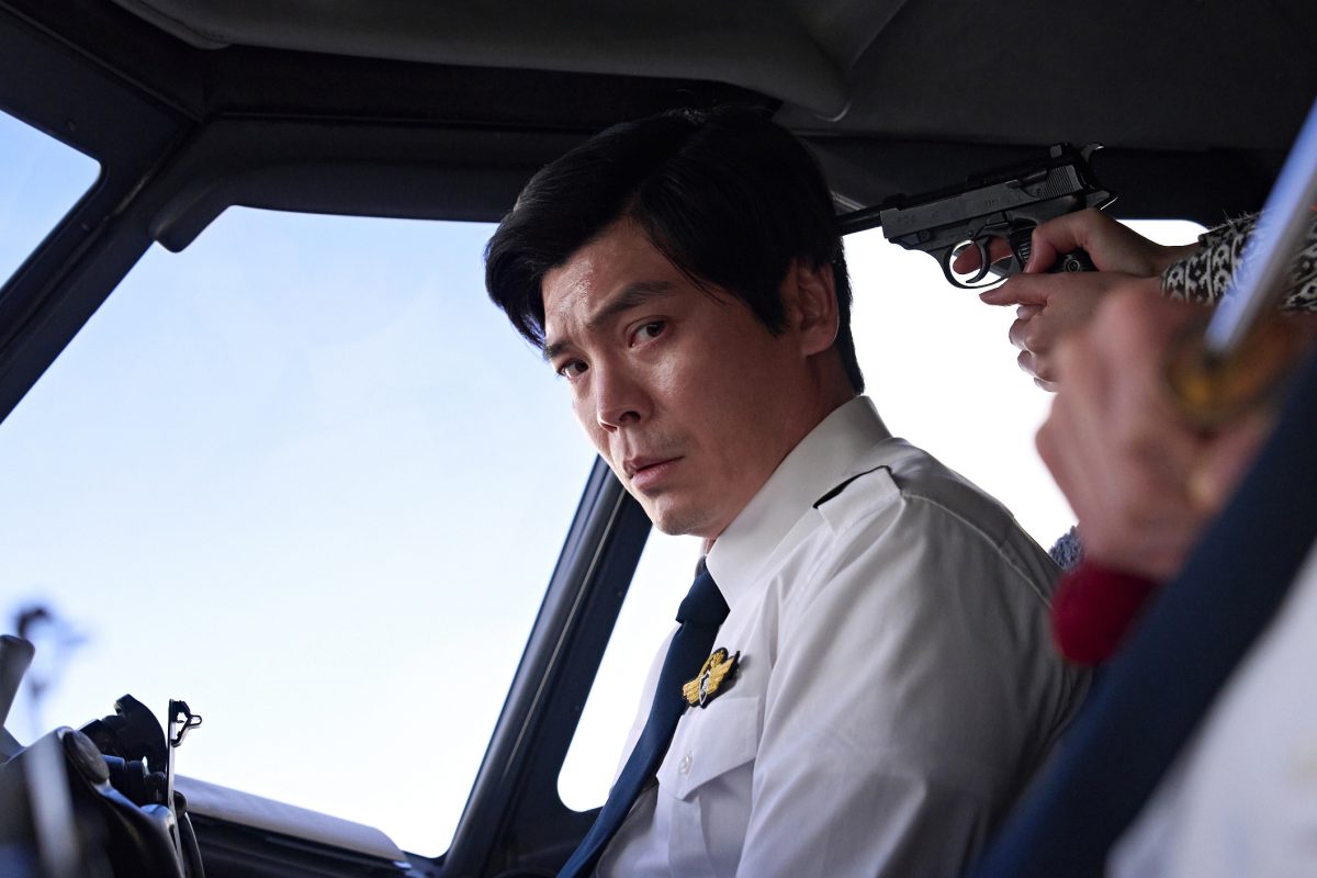 Byun Sung-hyun's Good News (Gut Nuiuseu, 2025) follows a plane hijack incident from over five decades ago. Yet, its satire of bureaucratic ineptitude is so potent that some might consider it a present-day event happening somewhere around us. The film falls in the vein of 'Dr. Strangelove,' which portrayed the sheer absurdity of political boardrooms. Byun's film uses a similar dark comedic tone to critique more than what meets the eye. So, while showing a botched hijack attempt by political activists, it underlines the glaring concerns about the authorities in charge of pacifying their voices without realizing or acknowledging their inherent flaws. The film also highlights the fabrication of reality by the supposed victors to present a narrative that suits their overarching motives. This comedic thriller, inspired by real events, is streaming on Netflix. Spoilers Ahead Good News (Gut Nuiuseu, 2025) Plot Summary & Movie Synopsis: 'Good News' centres around an event in 1970 when the Red Army Faction boarded a plane in Japan to divert it to Pyongyang, North Korea, in an attempt to make their voices heard.  What happens in Good News on Netflix? In 1970, a group of Red Army Faction members got on the plane from Haneda to Itazuke. They didn't need to go through security screenings or metal detectors because these things had not been mandatory until then. In Byun Sung-hyun's reenactment of this incident, Sho Kasamatsu plays the leader of the hijack group, while Nairu Yamamoto plays one of his associates, Asuka. Shortly upon arrival, they hijack the plane and threaten captain Takahiro Kubo and first officer Seigo Maeda to divert it to the North Korean airspace. The pilots realize the members' lack of knowledge about the plane and the destination, and use it to buy more time. As it happens, the ground base tries its best to pacify the situation. Captain Takahiro lands the plane at a Japanese airport, claiming they need to refuel. The Japanese authorities in charge claim that they need approval from the US Armed Forces. They use that time to rescue the passengers, but to no avail. Instead of pacifying the situation, they escalate it since the group members threaten to kill passengers if their demands are not met. Since Japanese leaders fail in this regard, the onus falls on the South Korean forces. That's when KCIA director Park Sang-hyeon (Ryoo Seung-bum) brings an enigmatic figure, dubbed Nobody (Sul Kyung-gu), to de-escalate the situation. As a Korean person, Nobody is not on board with helping the Japanese.  Yet, Park insists they help with this situation to protect their future ties with the US and not let the North have an upper hand in the economic matters they deem more important. As it happens, one of the hostages on the plane gets injured, leading some passengers to be evacuated. Yet, the plane remains on its way to the North, which puts Japan and South Korea in a bind since they don't have provisions for such a landing.  How does Nobody help with the hijack?  Nobody brings Air Force lieutenant Seo Go-myung (Hong Kyung) to help with the situation. He was the only Korean individual on the US fighter jet that survived an attack in the North Korean airspace. So, Nobody seeks his expertise in the system, dubbed RAPCON, to contact the hijackers. He forces Lieutenant Seo to break an aviation law for this secret operation. Then, the team tries to persuade the Faction members against landing in North Korea with a threat of fighter jets, but the members claim they are willing to be sacrificed. So, the team plans on an alternate strategy: they make the plane land in a South Korean airport, pretending it is landing in Pyongyang.  Lieutenant Seo manages it by pretending to be a North Korean officer. After that happens, the operation is not simply about the safety of the hostages; it's also about different authority figures trying to preserve their image. That's why nearly everyone in charge uses this mission to present themselves as kind-hearted saviors, but promote it only when the decisions suit their agenda. Initially, Lieutenant Seo believes the operation will gain him fame and glory, but the dream vanishes as soon as the plane lands in Kimpo, South Korea. The authorities try to paint it as a North Korean paradise that the Faction members consider it to be, but the facade gets exposed soon, putting them in further danger.  Thus, KCIA director Park readies Lieutenant Seo as the scapegoat. Throughout this operation, Park accepts his involvement only when it shows him as a hero. Otherwise, he throws Seo under the bus, hoping he bears the brunt. So, when the faction leader asks to meet him (the person who tricked them into this landing) in person, he sends Seo instead.  Good News (Gut Nuiuseu, 2025) 'Netflix' Movie Ending Explained: KCIA director Park compels Lieutenant Seo to enter the plane to pacify the hijackers. That's when Seo bonds with the Faction's leader over their love for a manga, dubbed 'Ashita na Joe.' It upsets Faction member, Asuka, who ends up stabbing the leader. Although this seems like an accident, it was a part of their mission. She stabs him at a spot where he won't suffer too much and survive a day if the bleeding is kept under control. While the members see it as a part of their greater goal, the passengers get traumatized by the incident. So, they urge Seo to get them to the North as a last resort for survival. Otherwise, a suicide bomber on the plane will kill them all in the next 24 hours.  Unlike them, the Japanese boardroom members feel no remorse in sending the passengers to the North because it would save them from guilt and accountability. So, in a dire attempt to save everyone, Lieutenant Seo makes the hijackers appear less threatening in their eyes. The next morning, South Korea's first lady (Jeon Do-yeon) arrives there at the request of boardroom officials. However, she is more concerned with portraying her chair in high regard, thus making an emotional plea to keep all the hostages safe without offering any constructive feedback as to how. So, the onus, once again, falls on Seo, who tries his best to convince the hijackers to let the remaining passengers leave.  What lies in Lieutenant Seo's fate?  In the end, Seo convinces the hijacker's leader not to die with a passionate plea involving their favorite manga character. Around this time, Nobody convinces the Japanese Deputy Minister (Takayuki Yamada) to sacrifice himself to protect the hostages. Once the hostages are rescued, the Faction members reach the North. After it all, every single involved nation resorts to positioning itself to suit its agenda. This is why Seo gets no credit for carrying out this operation of sacrificing himself more than once, since South Korea does not claim any involvement in these matters. So, he becomes the unsung hero of this operation while the deputy minister and the pilots end up taking the credit.  The point of this ending is not simply an innocent young officer's betrayal in the face of a behemoth or his efforts being left unacknowledged. Instead, the final moments reflect the film's critique of the nature of truth. It shows how 'truth,' in such cases, is often revealed to suit an agenda, irrespective of its connection to the objective reality.  Read More: Good News (Gut Nuiuseu, 2025) Movie Review: A Sharp Acerbic Intersection Of Ruthless Satire and Political Paranoia Good News (Gut Nuiuseu, 2025) Movie Trailer: Good News (Gut Nuiuseu, 2025) Movie Links: IMDb, Rotten Tomatoes, Wikipedia, Letterboxd Good News (Gut Nuiuseu, 2025)
